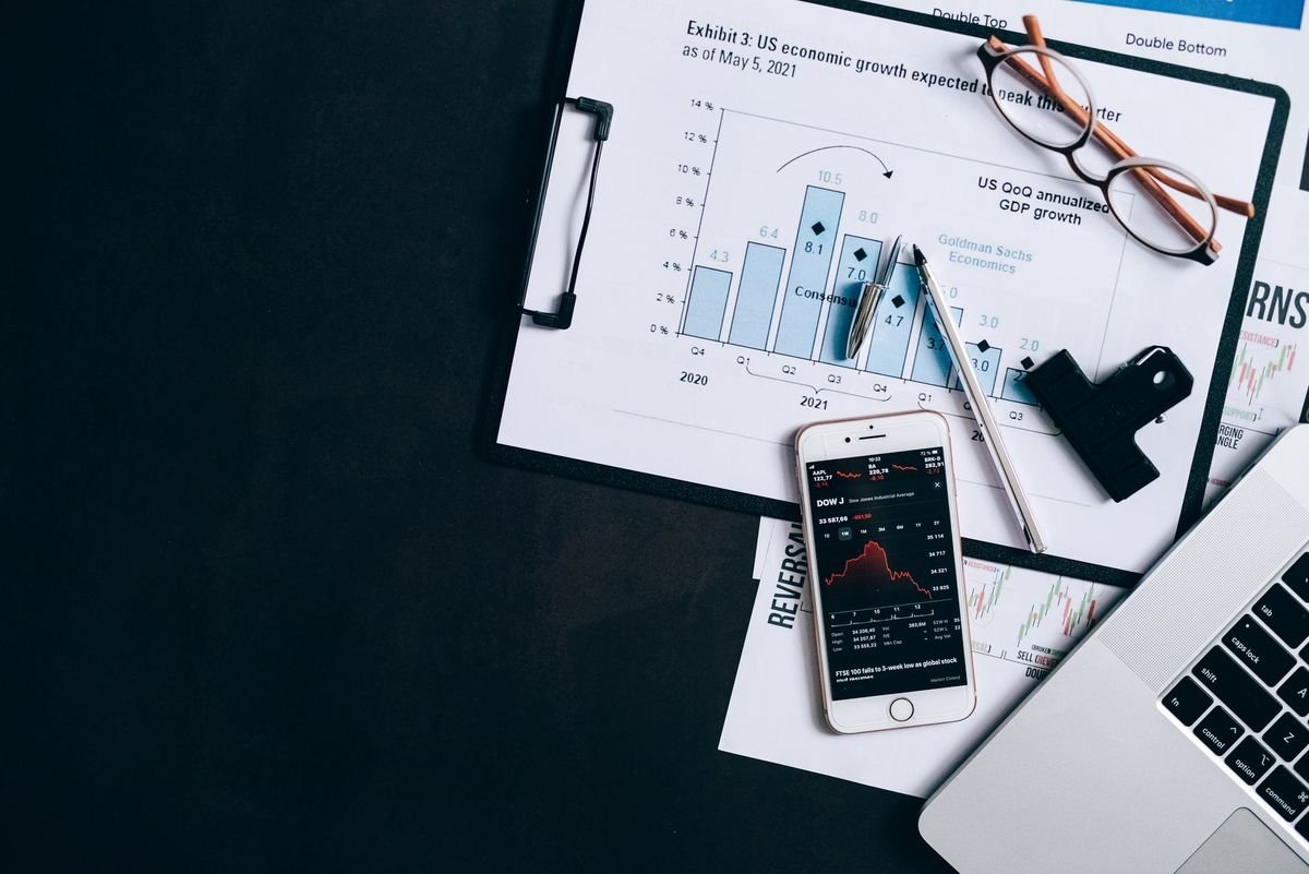 Top view of financial reports, smartphone showing stock market data, and a laptop on desk.