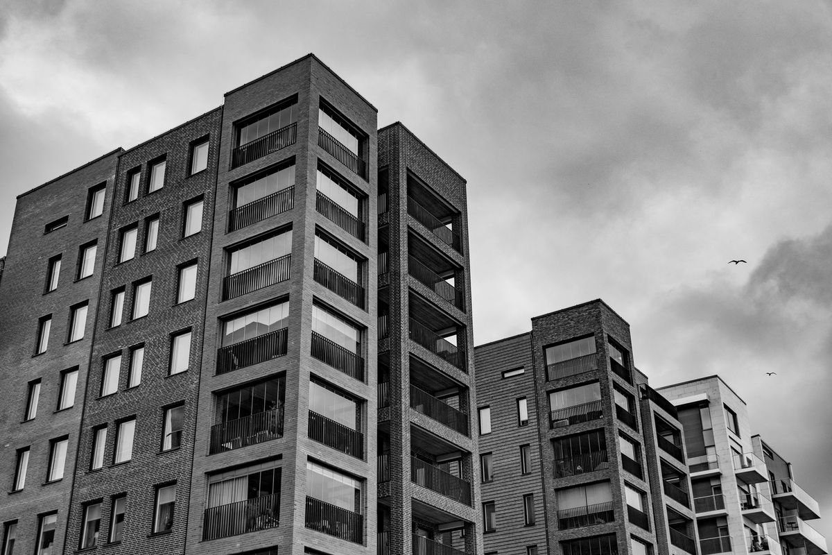 Black and white image of modern urban apartment buildings against a cloudy sky.