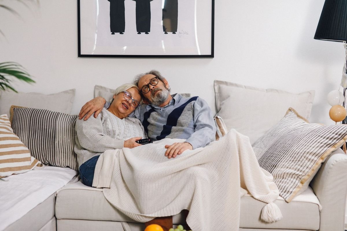 Senior couple sitting warmly together on a sofa, embracing in a cozy living room.